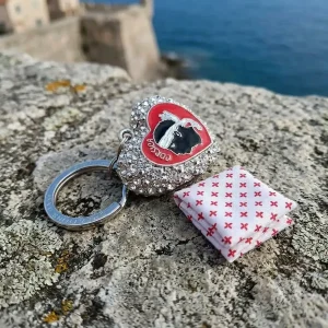 Porte-clés souvenir de Corse : cœur en métal argenté orné de strass, avec le symbole de la tête de Maure et le texte "Corsica" au centre. Anneau d'attache gravé.
