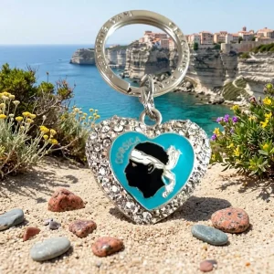 Porte-clés souvenir de Corse : cœur en métal argenté orné de strass, avec le symbole de la tête de Maure et le texte "Corsica" au centre. Anneau d'attache gravé.