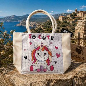 Sac cabas enfant en toile illustré d'une licorne rose avec la mention So Cute, posé dans le maquis corse.