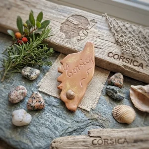 Magnet Corse en argile fait main posé sur de la pierre avec coquillages, bois flotté et symbole de la tête de maure