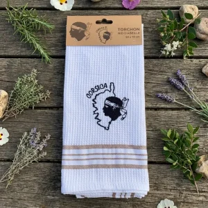 Torchon de cuisine blanc en nid d'abeille avec une broderie noire représentant la carte de la Corse, la Tête de Maure et l'inscription "Corsica". Le bas est orné de rayures coloris marron. Le torchon est présenté plié